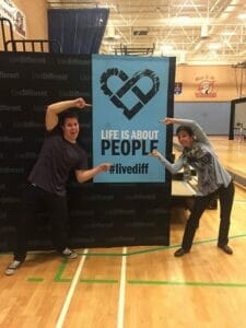 Two people pose with 'Life is about people' banner.