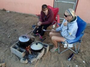 Two women cooking outdoor on a small campfire.