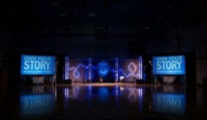 Stage with 'Own Your Story' signs and spotlight.