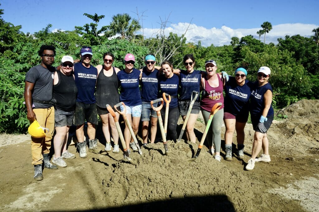 Group of volunteers holding shovels on dirt pile.