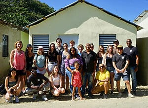 Diverse group standing in front of a small house.