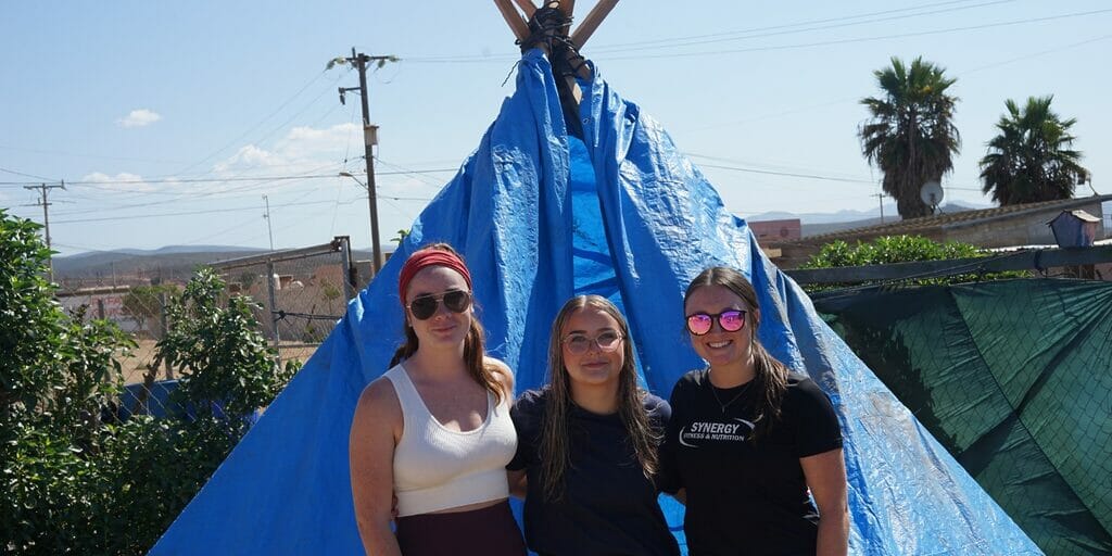 Three women smiling in front of a blue tent.