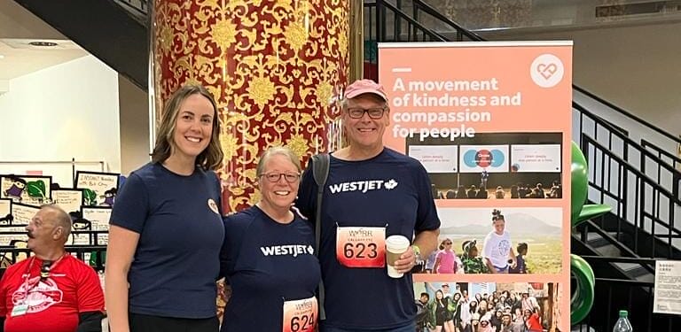 Three people in front of kindness banner at event.