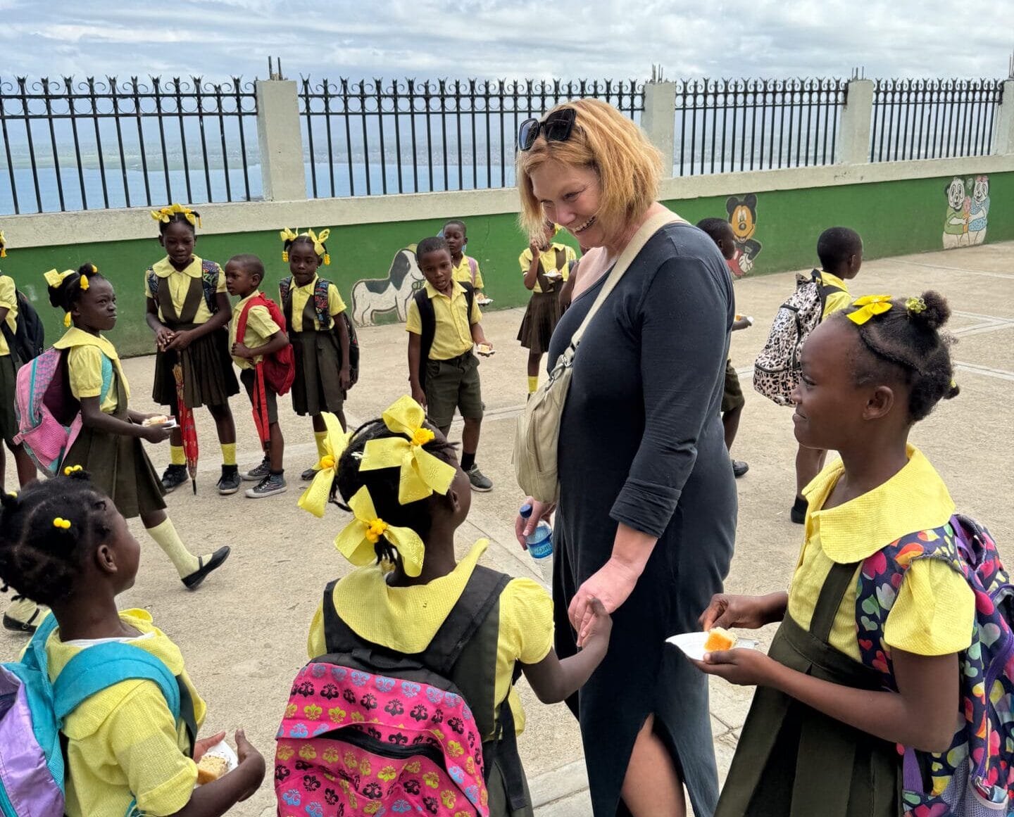 Woman interacting with children in school uniforms outside.