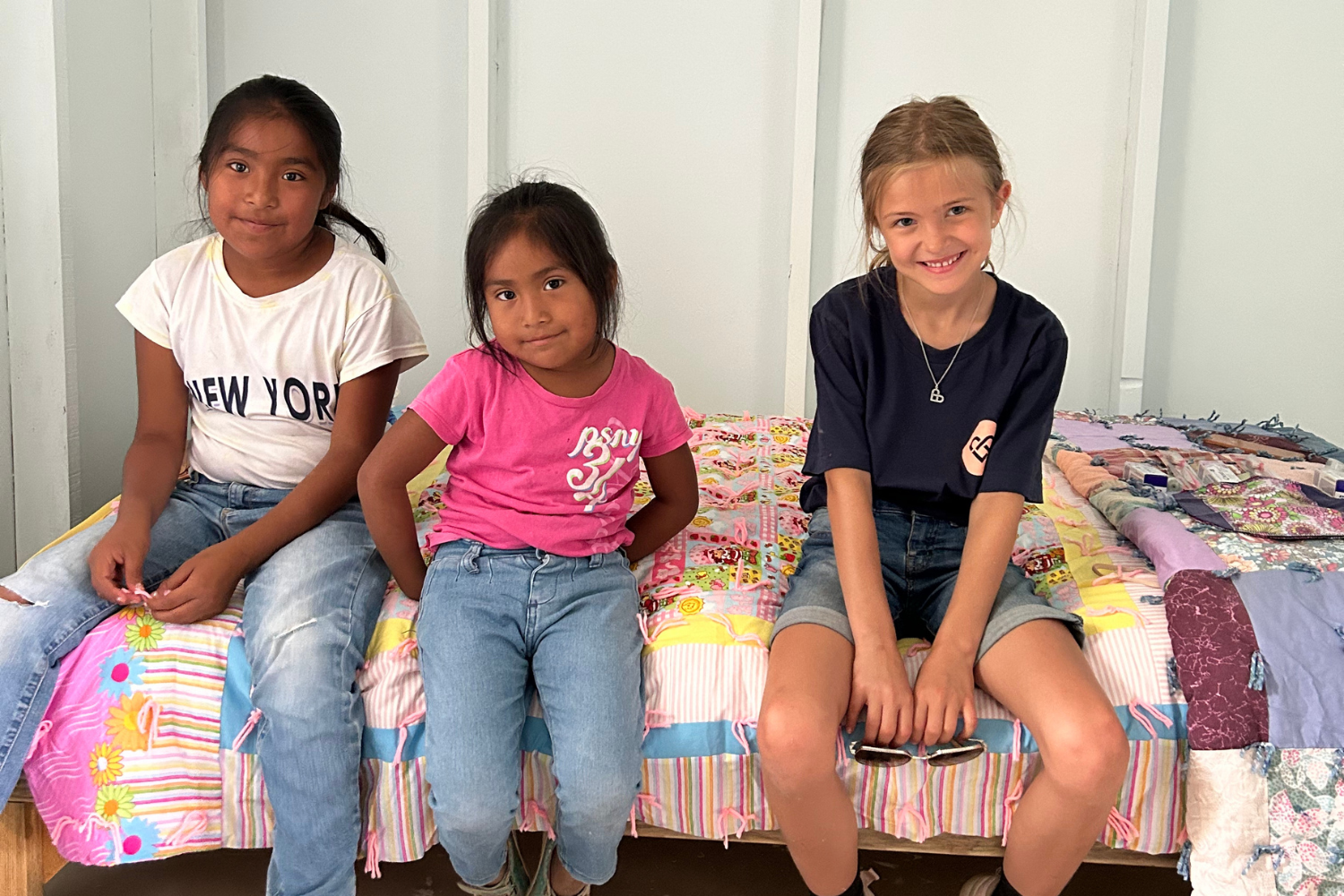 Three girls sitting on a colorful bed smiling.